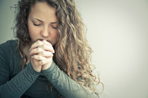 Girl with laced fingers and eyes closed in prayer.