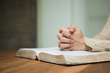 a woman with praying hands over an open Bible 