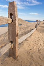 Wooden fence posts and rails on the sand at the beach, near the ocean.