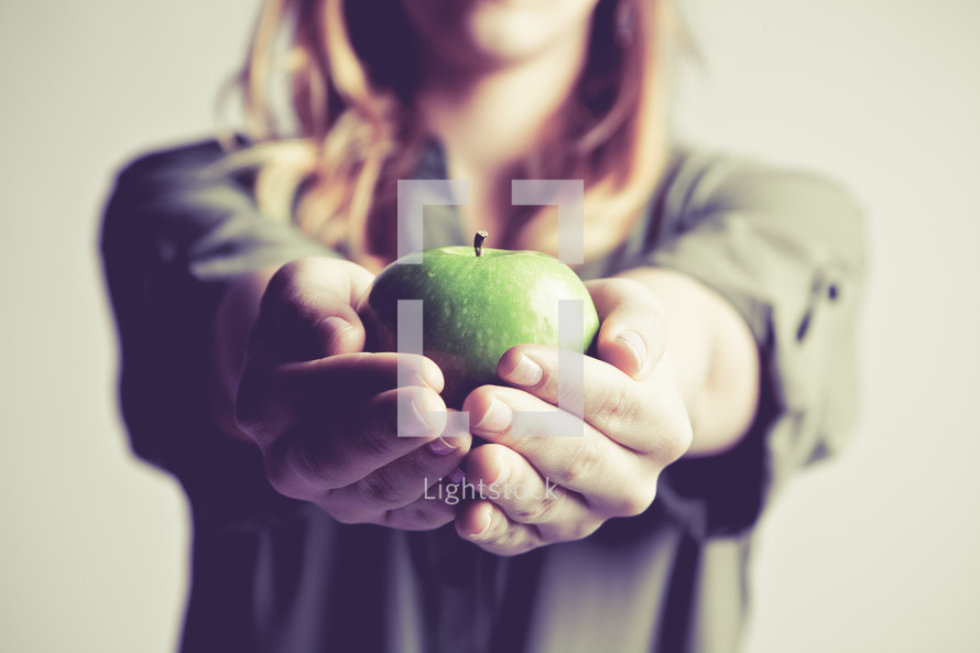 woman holding out a green apple