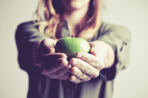 woman holding out a green apple