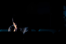 man sitting in a dark empty church with his head bowed in prayer