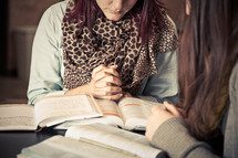 young women in prayer over Bibles at a Bible study