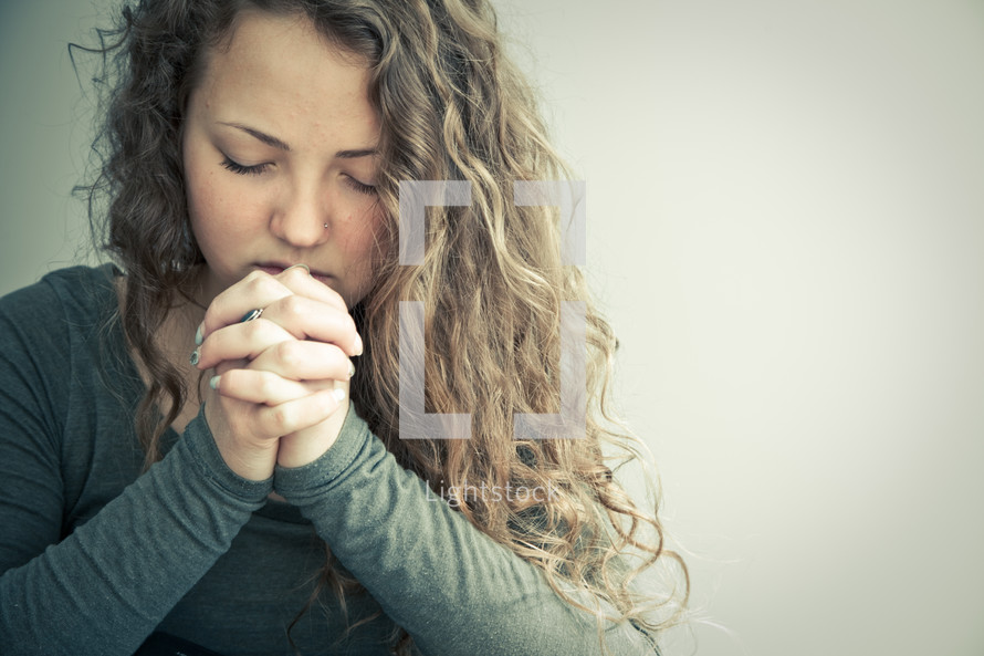 Girl with laced fingers and eyes closed in prayer.