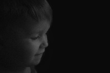 face of a young boy standing in a dark room 