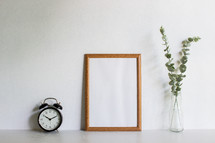 alarm clock, blank frame, and vase with eucalyptus 