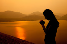 a woman praying by a lake at sunset 