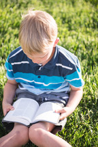 a boy reading a Bible in the grass 
