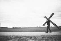 man carrying a large cross along the highway - re-enacting Christ's walk, bearing the cross