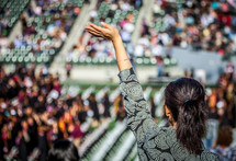 a woman in the audience with a raised hand at a graduation ceremony.