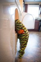 toddler boy in pjs looking in a dryer 