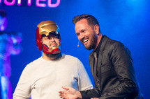 a minister on stage with a man dressed as a super hero 