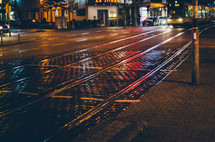 night lights reflect on a rainy city street with tram tracks