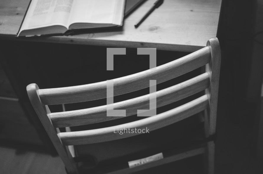 A chair at a desk with a pen and bible