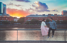 a couple sitting on a railing in front of a river 