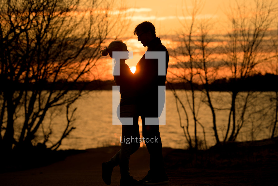 a couple standing together by a lake at sunset 