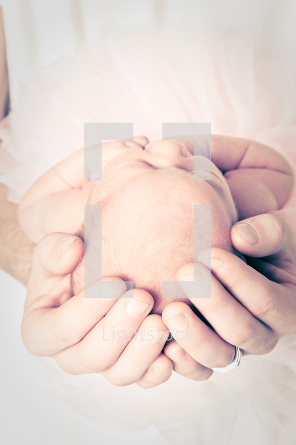 father's hands cradling a newborn infant