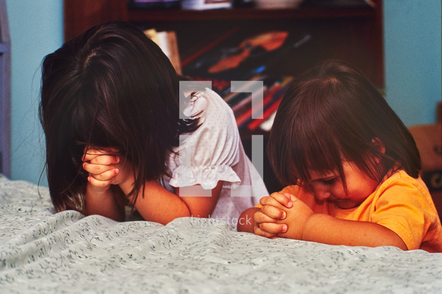 little girls praying over a bed 