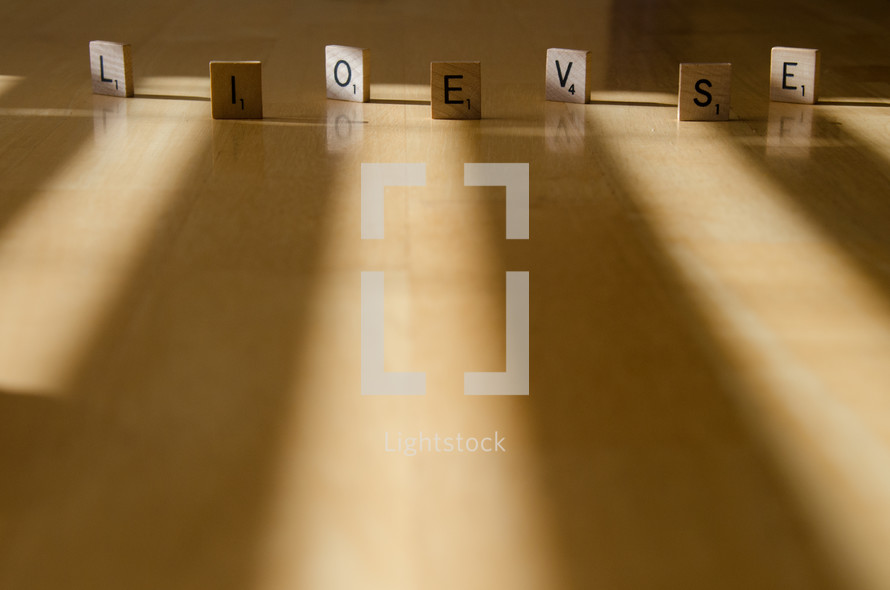"Love" and "lies" spelled out with Scrabble tiles and arranged  in strips of light and shadow.