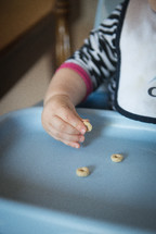 an infant in a highchair eating Cheerios 