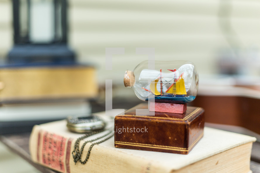 A book, pocket watch, wooden box, ship in a bottle, on a table.