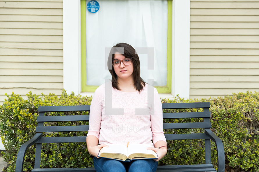 A woman sits on a bench with an open Bible in her lap.