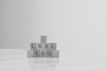 "I love you" spelled in stacked scrabble tiles in black & white.