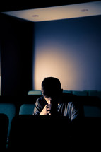 man sitting in a dark empty church praying 