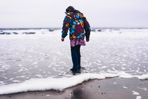 a child in a coat and boots walking on a shore 