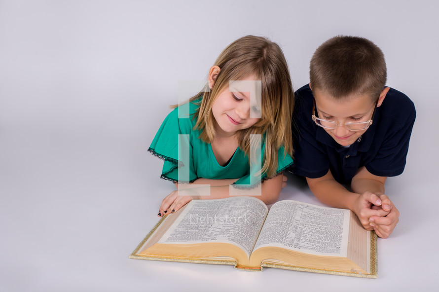 Siblings reading the Bible together on the floor.