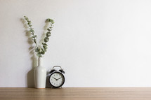 vase and alarm clock against a plain white wall 