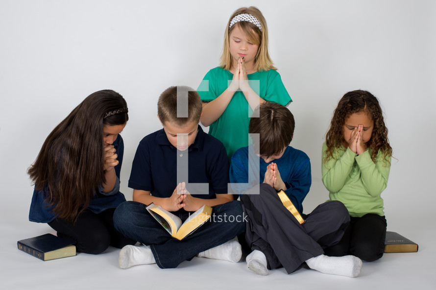 Children praying together over the Bible.