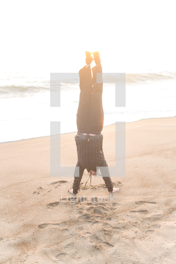 man doing a handstand on a beach 