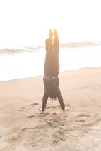 man doing a handstand on a beach 