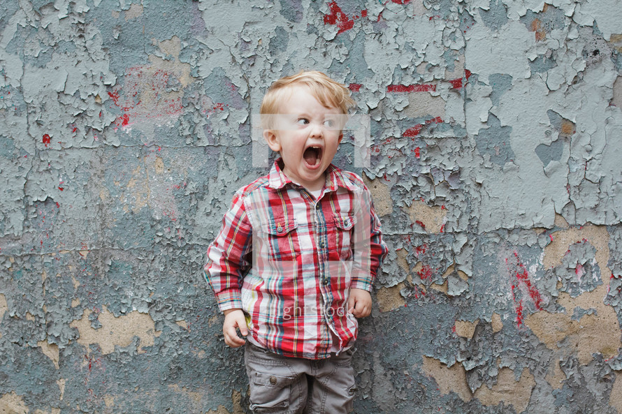 boy child yelling in front of a wall with peeling paint 