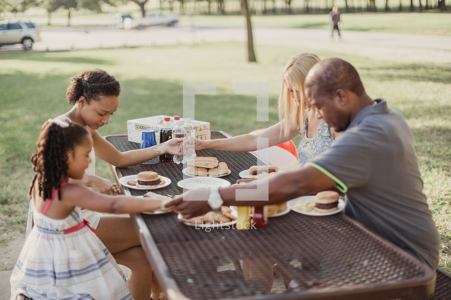 family holding hands in prayer at a picnic table outdoors 