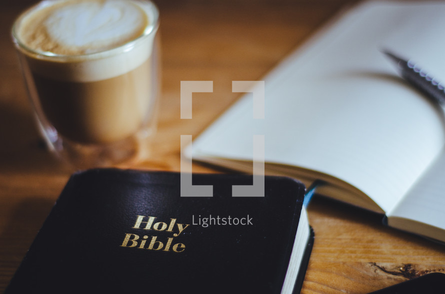 A bible, coffee and open notebook on a table