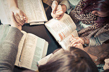 women holding hands in prayer over Bibles