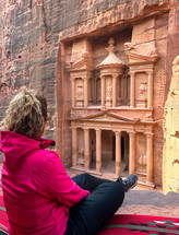Ancient Petra in Jordan. Seated tourist from behind looking at the ruins.