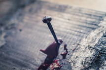 A bloody nail hammered into a wooden cross beam