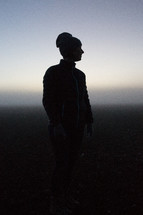silhouette of a woman standing outdoors in a beanie 