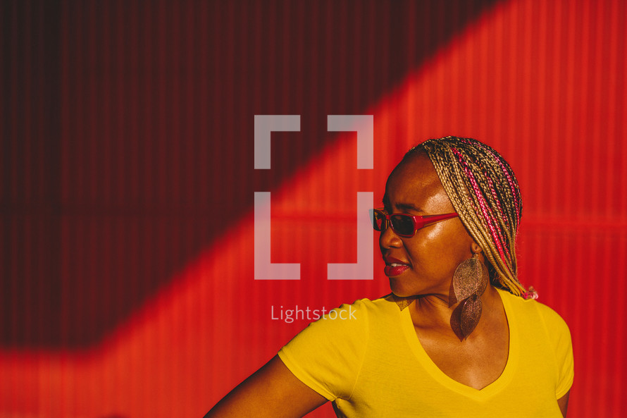 African-American woman standing in front of a red wall wearing sunglasses 