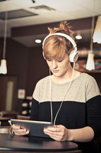 young woman looking at an iPad with headphones on