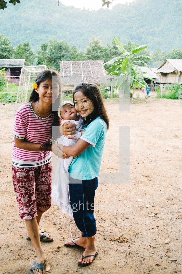 little girls holding a newborn baby in a village 