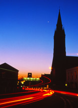 headlights and taillights from a freeway at night and silhouette of a steeple  