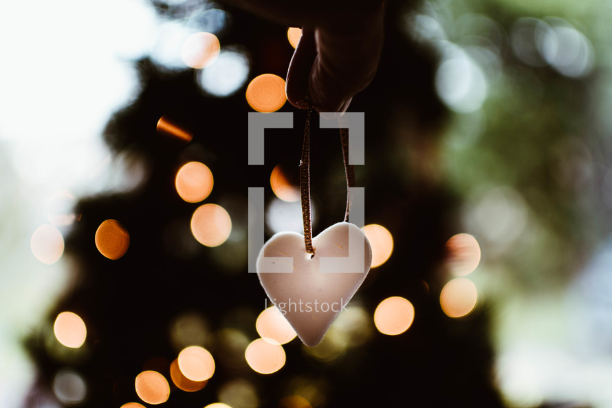 hand holding a heart ornament and bokeh Christmas lights 