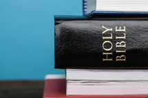 A Bible in the middle of a stack of books.