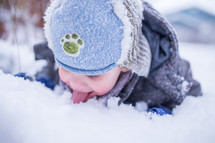a boy child playing outdoors in snow and licking snow 