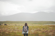 a young woman standing in a field with a backpack 
