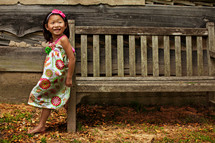 girl child in a dress leaning on a wood bench